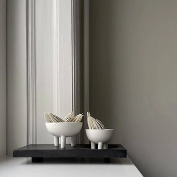 Two modern white 101 Copenhagen Duck Bowl Minis with vertical legs, each holding folded napkins, sit on a black rectangular tray against a minimalist light gray wall—a striking home decor piece from 101 Copenhagen.
