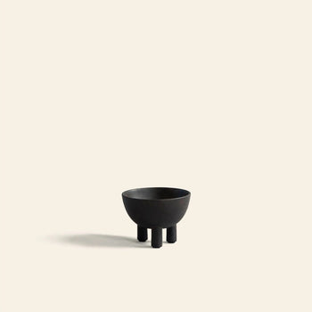 The 101 Copenhagen Duck Bowl, Mini by 101 Copenhagen is a small, matte black bowl with three short legs, centered on a light beige background and casting a soft shadow—an elegant addition to modern home decor.