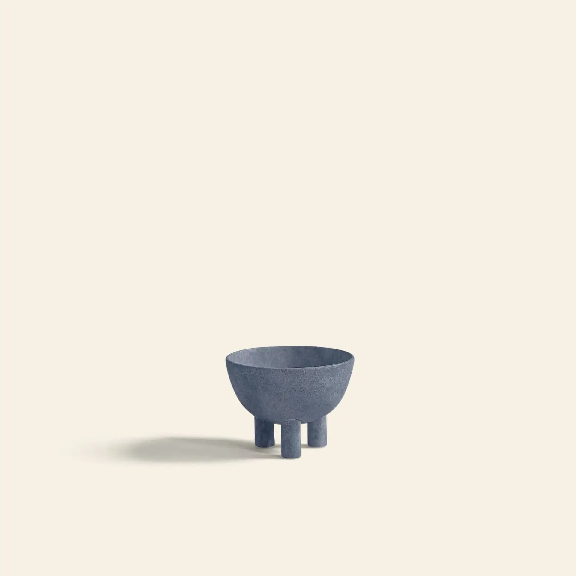 A minimalist photo of the 101 Copenhagen Duck Bowl, Mini—a small blue-gray bowl with three cylindrical legs—crafted by 101 Copenhagen for modern decor, placed on a light beige background with a soft left shadow.