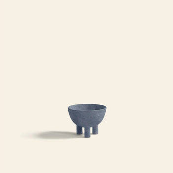 A minimalist photo of the 101 Copenhagen Duck Bowl, Mini—a small blue-gray bowl with three cylindrical legs—crafted by 101 Copenhagen for modern decor, placed on a light beige background with a soft left shadow.