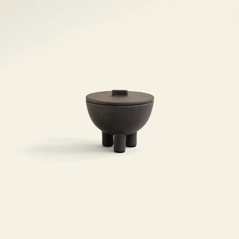 The 101 Copenhagen Duck Jar, Medio by 101 Copenhagen is a small, dark hand-glazed jar with a round lid and three cylindrical legs—ideal as a decorative storage piece—shown here against a light background.