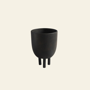 The 101 Copenhagen Duck Pot by 101 Copenhagen is a black, rounded, matte-finish planter with three short cylindrical legs, showcasing Scandinavian design against a plain off-white background.