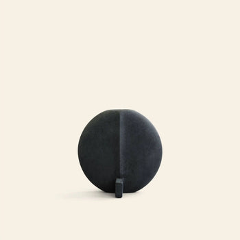 The 101 Copenhagen Guggenheim Vase, Petit by 101 Copenhagen features a round, matte black design with a flat base and small vertical support, set against a light beige background and reflecting subtle art deco influences.