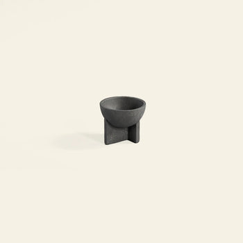 The 101 Copenhagen Osaka Bowl, Mini by 101 Copenhagen is a small modern black fiber concrete bowl with a round top and geometric cross-shaped base, shown against a plain light beige background.