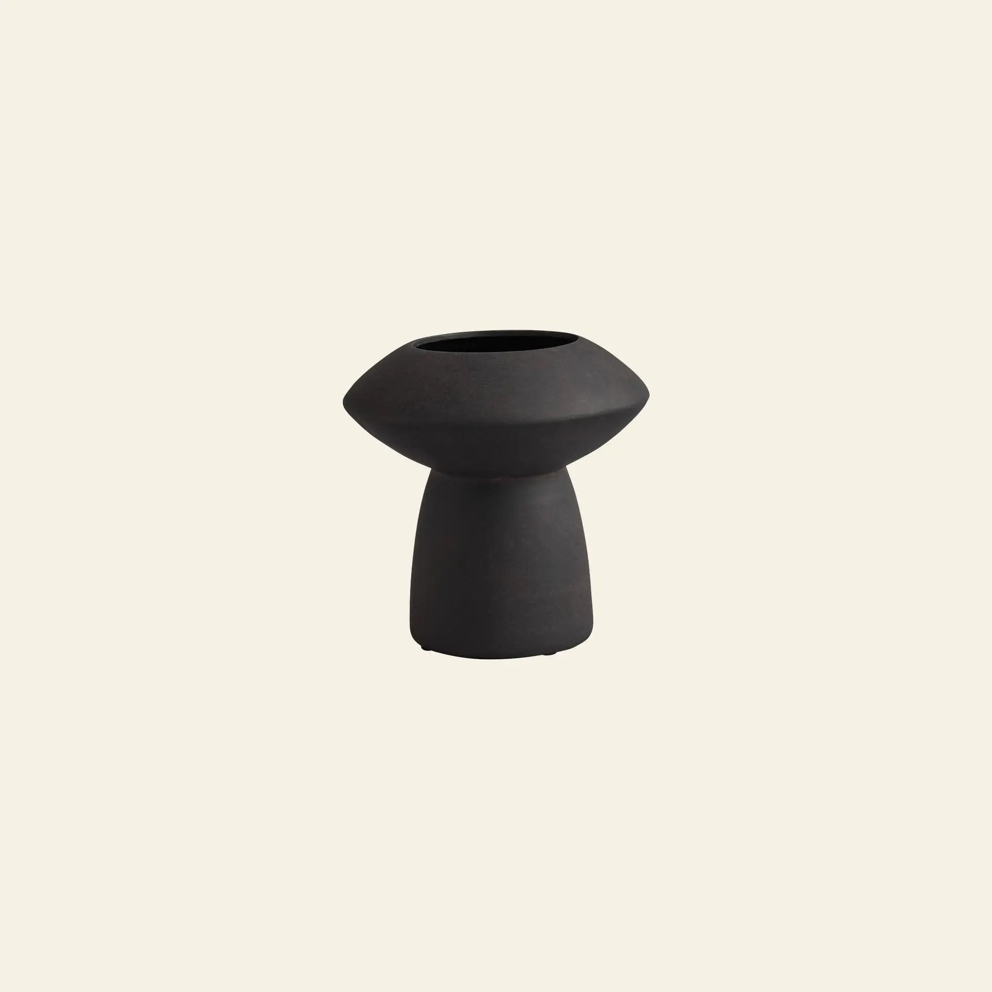 The 101 Copenhagen Sphere Vase Fat by 101 Copenhagen is a small, black vase featuring a wide, rounded top and narrow cylindrical base, exuding timeless elegance against a plain light beige background.