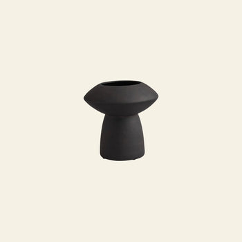 The 101 Copenhagen Sphere Vase Fat by 101 Copenhagen is a small, black vase featuring a wide, rounded top and narrow cylindrical base, exuding timeless elegance against a plain light beige background.