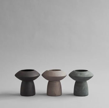The 101 Copenhagen Sphere Vase Fat by 101 Copenhagen, shown in black, taupe, and dark teal, features a modern geometric design with a rounded top and narrow cylindrical base—an elegant centerpiece against any light gray backdrop.