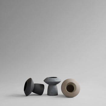 Four minimalist, geometric ceramic vases—including the 101 Copenhagen Sphere Vase Fat—by 101 Copenhagen in gray and beige sit in a row on a light gray backdrop, creating a captivating and timelessly elegant centerpiece.