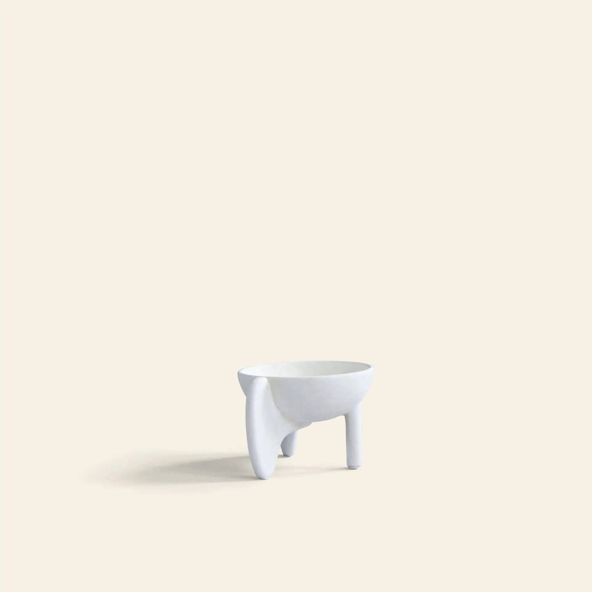 The 101 Copenhagen Wing Bowl, Mini by 101 Copenhagen is a small, minimalist white sculptural bowl with three uneven legs, crafted from fiber concrete and displayed on a light beige background.