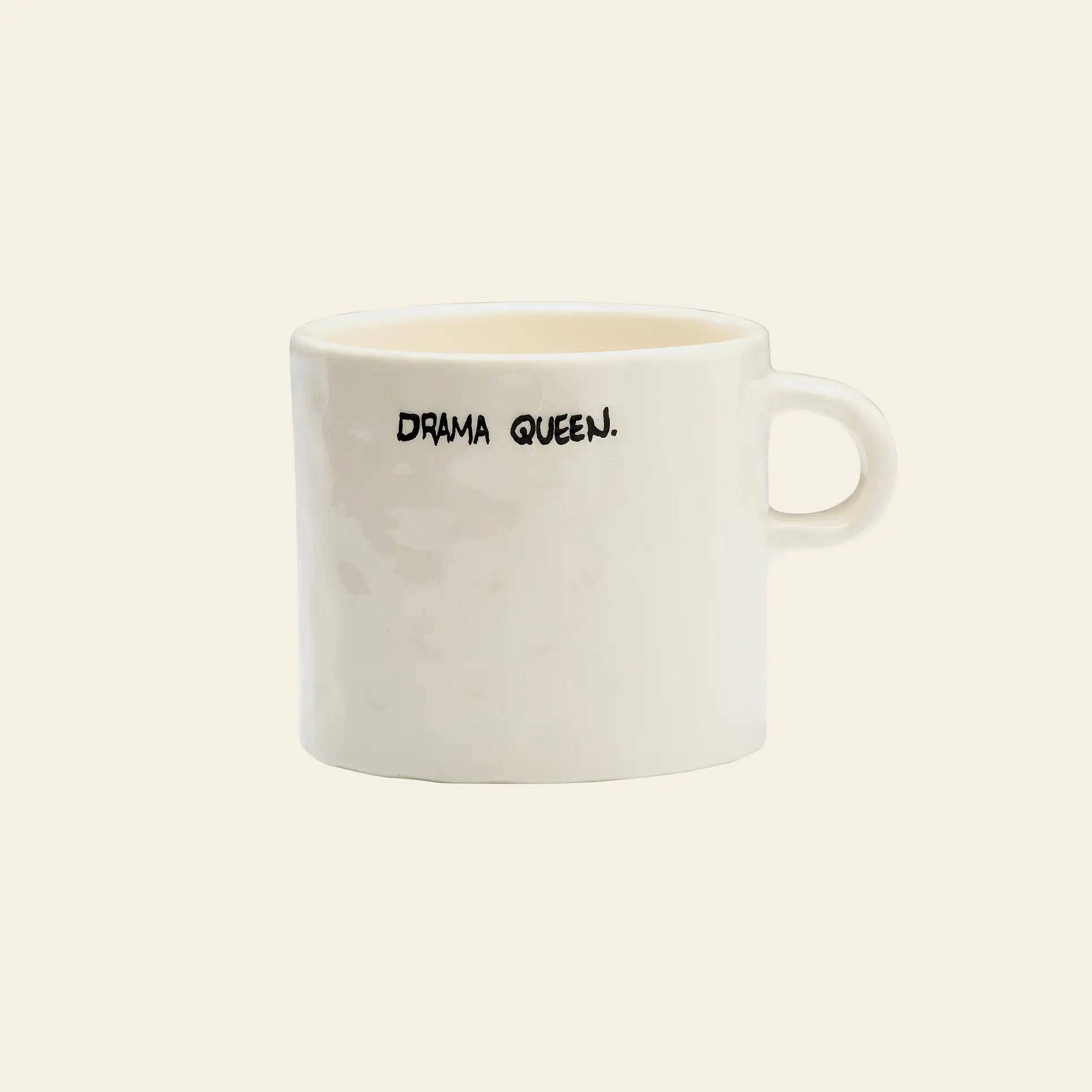 The Anna + Nina Drama Queen Mug features bold black lettering and a round handle, adding theatrical flair to your coffee breaks. Set against a plain light background, this white mug is perfect for expressive personalities.