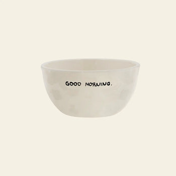 The Anna + Nina Good Morning Bowl by Anna + Nina is a simple off-white ceramic breakfast bowl featuring GOOD MORNING. in bold black uppercase letters on the side, displayed against a plain light background.