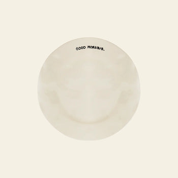 The Anna + Nina Good Morning Breakfast Plate by Anna + Nina features “GOOD MORNING.” in black near the rim, viewed from above on a plain off-white background—a cheerful upgrade to your breakfast routine.