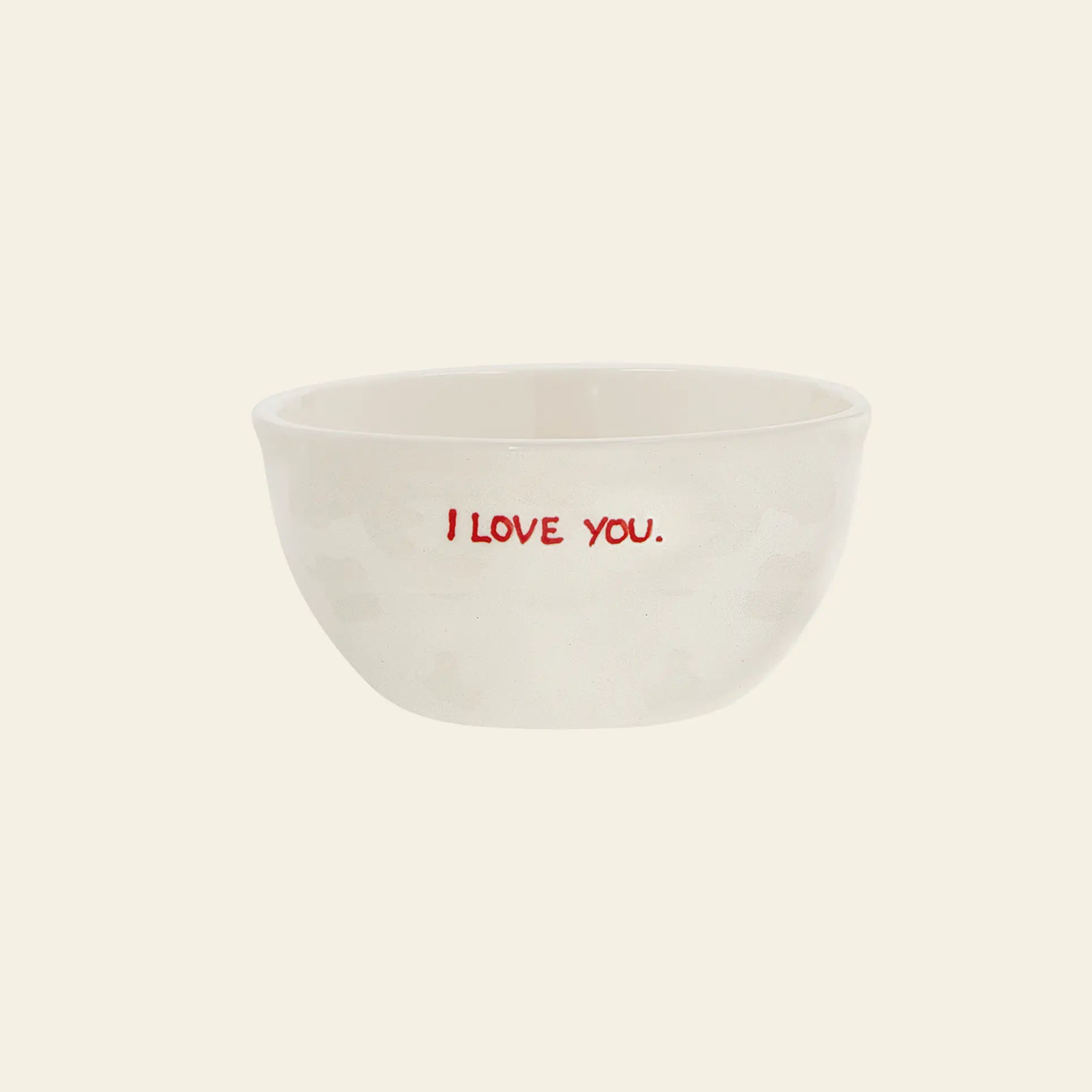 The Anna + Nina I Love You Bowl is a small white ceramic bowl from Anna + Nina, featuring I LOVE YOU. in red on the front—perfect for breakfast and displayed against a plain, light background.
