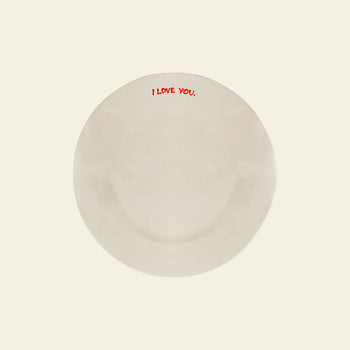 The Anna + Nina I Love You Breakfast Plate features I LOVE YOU. in bold red letters along the rim—ideal for breakfast in bed. The background is light beige, and its a charming ceramic piece from Anna + Nina.