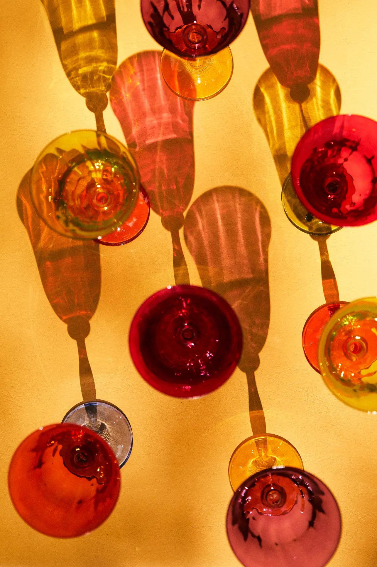 The Anna + Nina Multicoloured Wine Glasses, Set of 4, feature a vintage design and cast vibrant shadows on a yellow surface—an ideal housewarming gift from Anna + Nina.