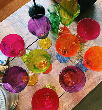 The Anna + Nina Multicoloured Wine Glasses, Set of 4, feature translucent shades of pink, green, yellow, and orange arranged on wood—an artistic and vibrant vintage-inspired design from Anna + Nina, perfect for a housewarming gift.