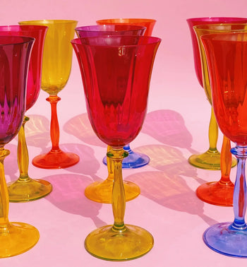 The Anna + Nina Multicoloured Wine Glasses, Set of 4, features vibrant red, yellow, blue, and orange stems and bowls—ideal as a housewarming gift or to bring vintage style from Anna + Nina to your table.