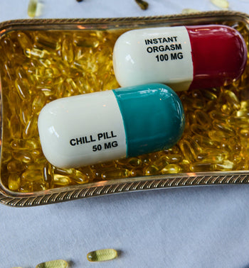 The Anna + Nina Chill Pill Figure by Anna + Nina features large novelty capsules in a playful, multicoloured design, making a fun decorative piece displayed among yellow capsules on a white tablecloth.