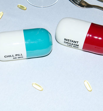 The Anna + Nina Chill Pill Figure features two large capsules—one labeled INSTANT ORGASM 100 MG—surrounded by small yellow capsules. The multicoloured design pops on a white surface, with a fork partially visible in the scene.