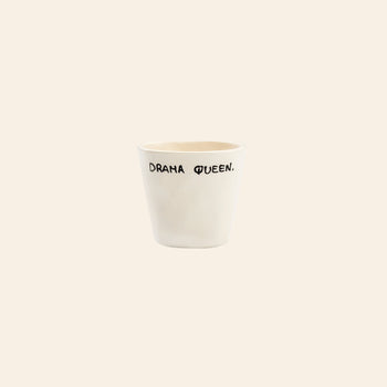 The Anna + Nina Drama Queen Espresso Cup is a white ceramic cup with DRAMA QUEEN. in playful black lettering on a light beige background—a bold, stylish touch for your coffee moments.