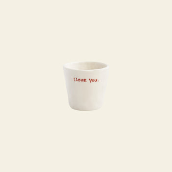 The Anna + Nina I Love You Espresso Cup is a white ceramic espresso cup with I love you. in red on the front, set against a light beige background—an ideal thoughtful gift from Anna + Nina.