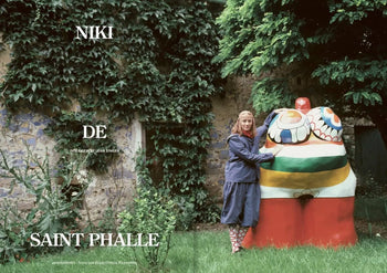 A woman in a blue dress and patterned boots embraces an abstract sculpture in a lush garden, with a stone wall behind her. Large white text reads Apartamento, echoing the style of Apartamento Magazine Issue #28s cover.