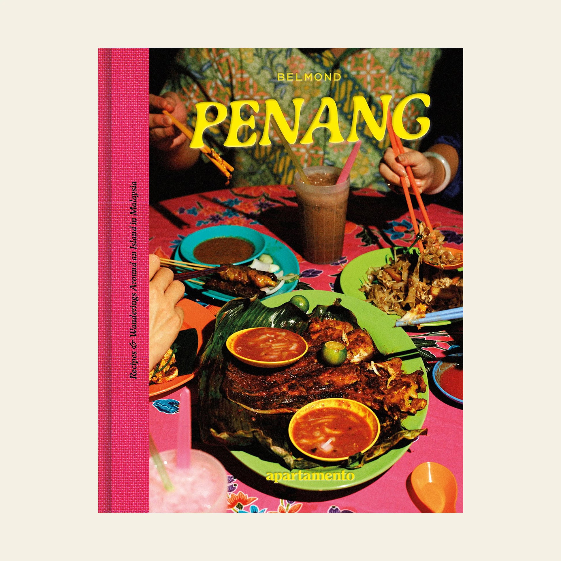The cover of Apartamento PENANG: Recipes & Wanderings Around an Island in Malaysia features hands enjoying vibrant Malaysian dishes and drinks on a pink table, with the Apartamento brand at the bottom.
