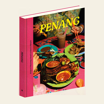 Apartamento PENANG: Recipes & Wanderings Around an Island in Malaysia by Apartamento features a pink spine and vibrant cover, inviting you to explore Malaysian cuisine—satay, sauces, rice, and iced drinks—across a bright table.