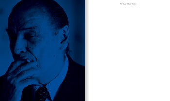 A man in a suit, his face shadowed and tinted blue, holds a cigarette to his mouth—evoking the enigmatic style of Xavier Corberó—on the cover of Apartamento The House of Xavier Corberó by Apartamento; the right page is blank with small black text at the top.