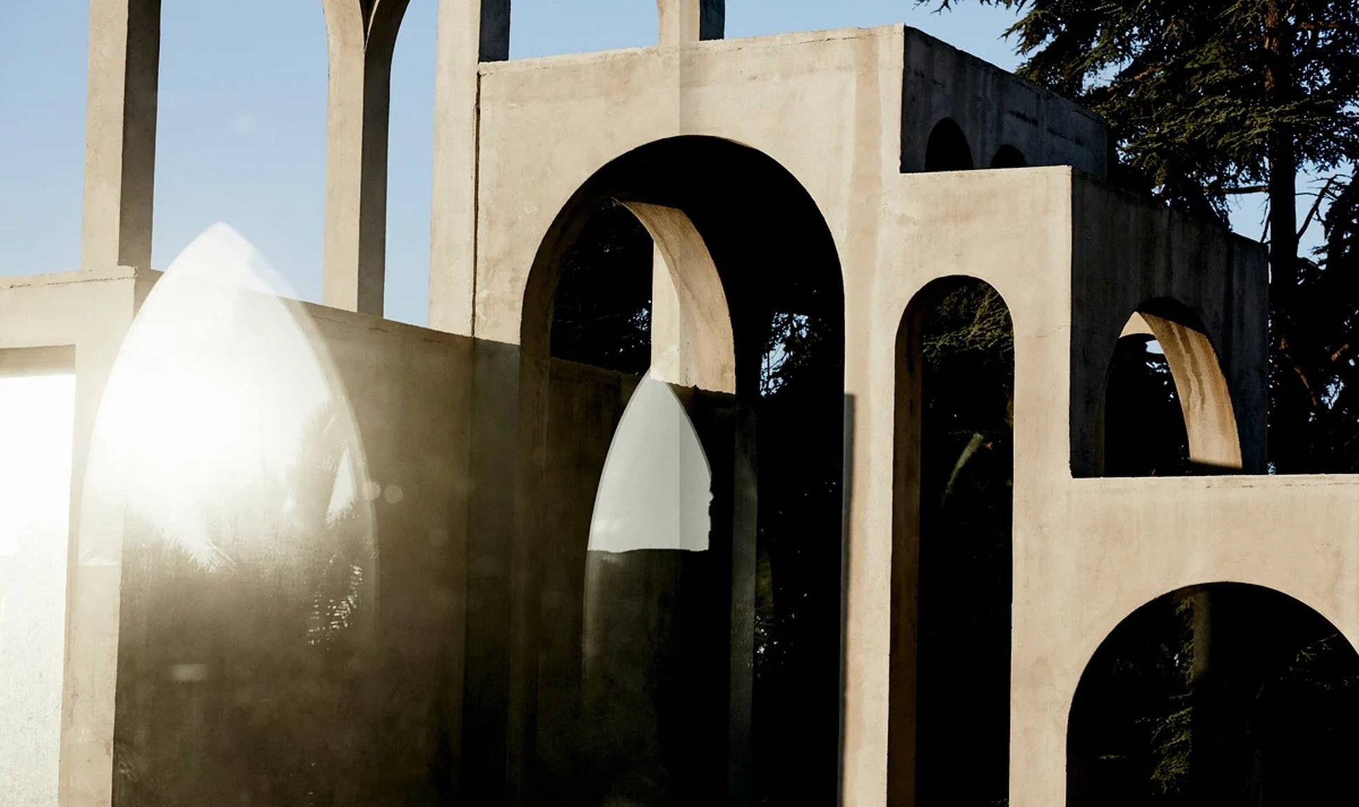 Sunlit concrete arches and geometric forms cast sharp shadows, while a reflective surface reveals a faint silhouette—evoking the surrealist style featured in Apartamento The House of Xavier Corberó by Apartamento.