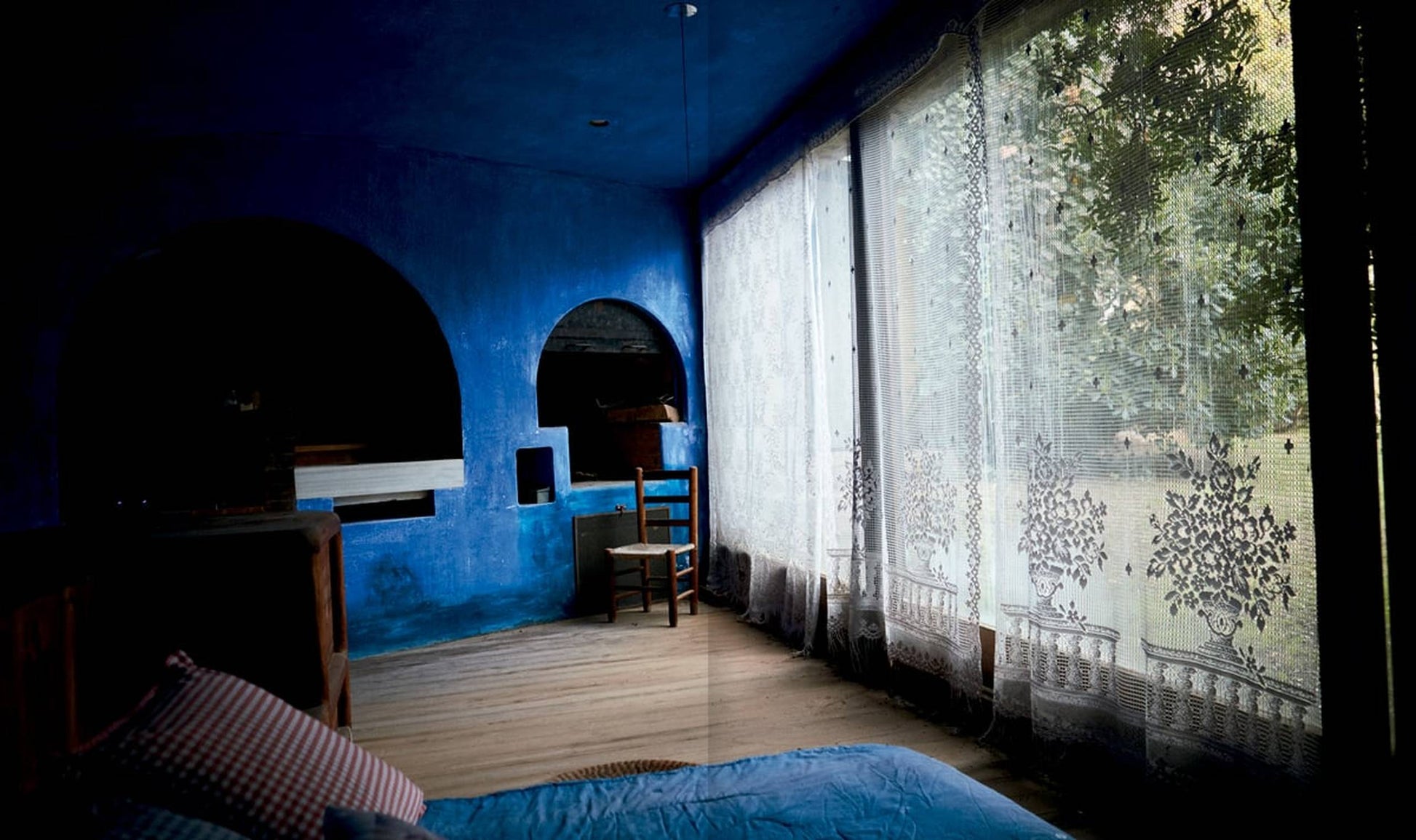 Apartamento The House of Xavier Corberó by Apartamento features a cozy Esplugues de Llobregat interior with deep blue walls, wooden floors, and sheer lace curtains recalling the surreal ambiance of Corberó’s iconic sculptures.