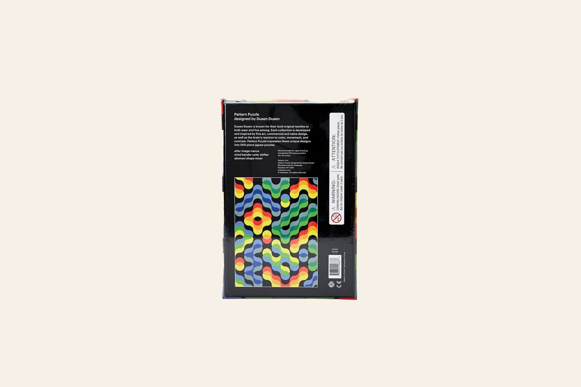 The image displays the back of the Areaware Dusen Dusen - Pattern Puzzle box, featuring a colorful wavy geometric design, text, and a barcode on a black background. This 500-piece puzzle is ideal for design enthusiasts.
