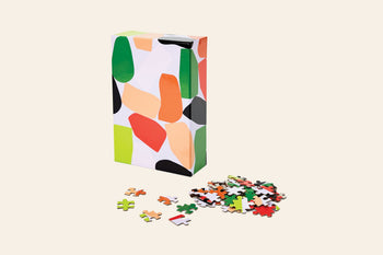 The Areaware Dusen Dusen - Pattern Puzzle by Areaware features 500 abstract pieces, ideal for design lovers, displayed upright with scattered pieces on a light beige background.