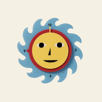 The Areaware Everybody Clock by Areaware features a yellow, sun-shaped face with bold numbers at 3, 6, 9, and 12. Its cheerful design includes black eyes, a triangular nose, and blue wave-like accents for a vibrant touch.