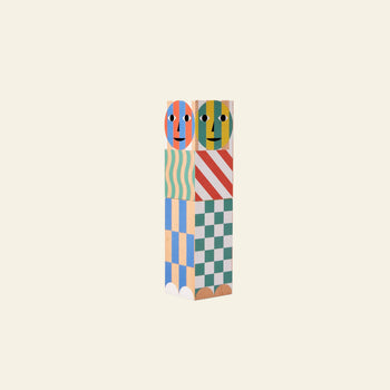 Two colorful Areaware Everybody Grinders by Areaware, stacked vertically with painted faces and playful patterns like stripes and waves, resemble whimsical kitchen tools against a plain cream background.