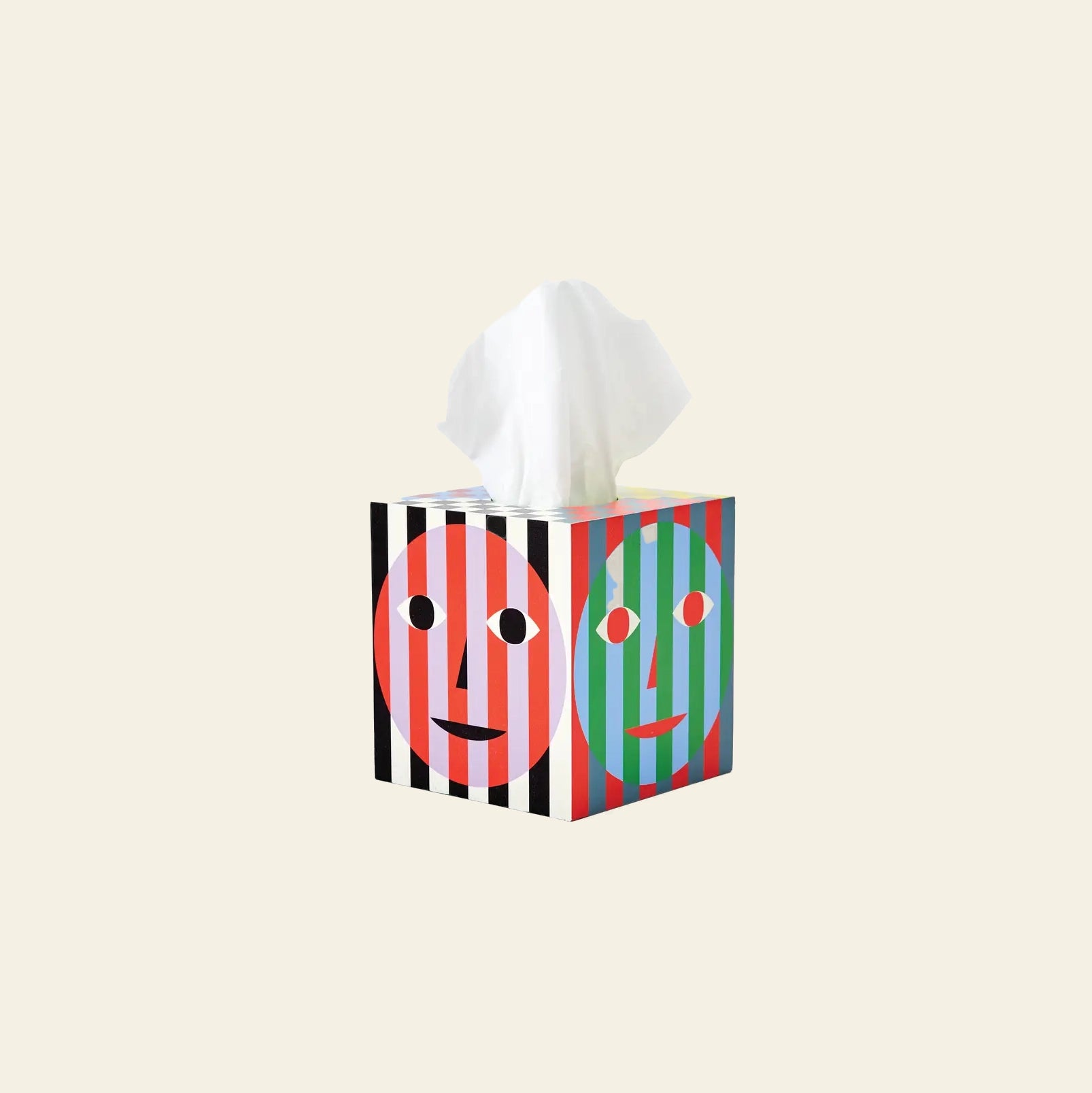 The Areaware Everybody Tissue Box features bright stripes and two stylized faces—one red, one green—with a white tissue peeking out, all set against a plain beige background.