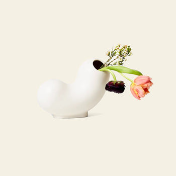 The Areaware Kirby Vase Curly by Areaware, a modern white ceramic vase with an abstract shape, displays pink, orange, and dark purple tulips plus small white blossoms—a striking floral arrangement ideal for stylish home decor.