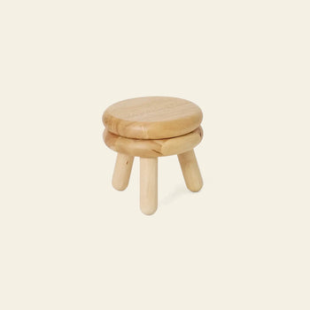 The Areaware Pluma Stool Short by Areaware features a small, round wooden seat atop three legs in light-colored wood. Its contemporary design suits any space and is shown here against a plain beige background.