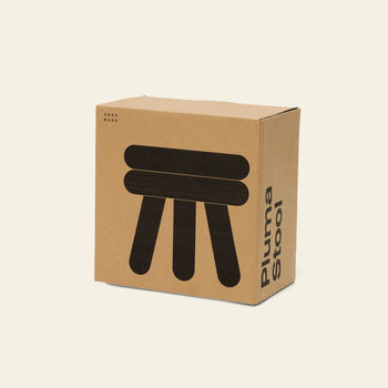A cardboard box labeled “Areaware Pluma Stool Short” with a minimalist black illustration of a three-legged stool on the front—echoing Areaware’s modern style and the stool’s versatile, contemporary design.