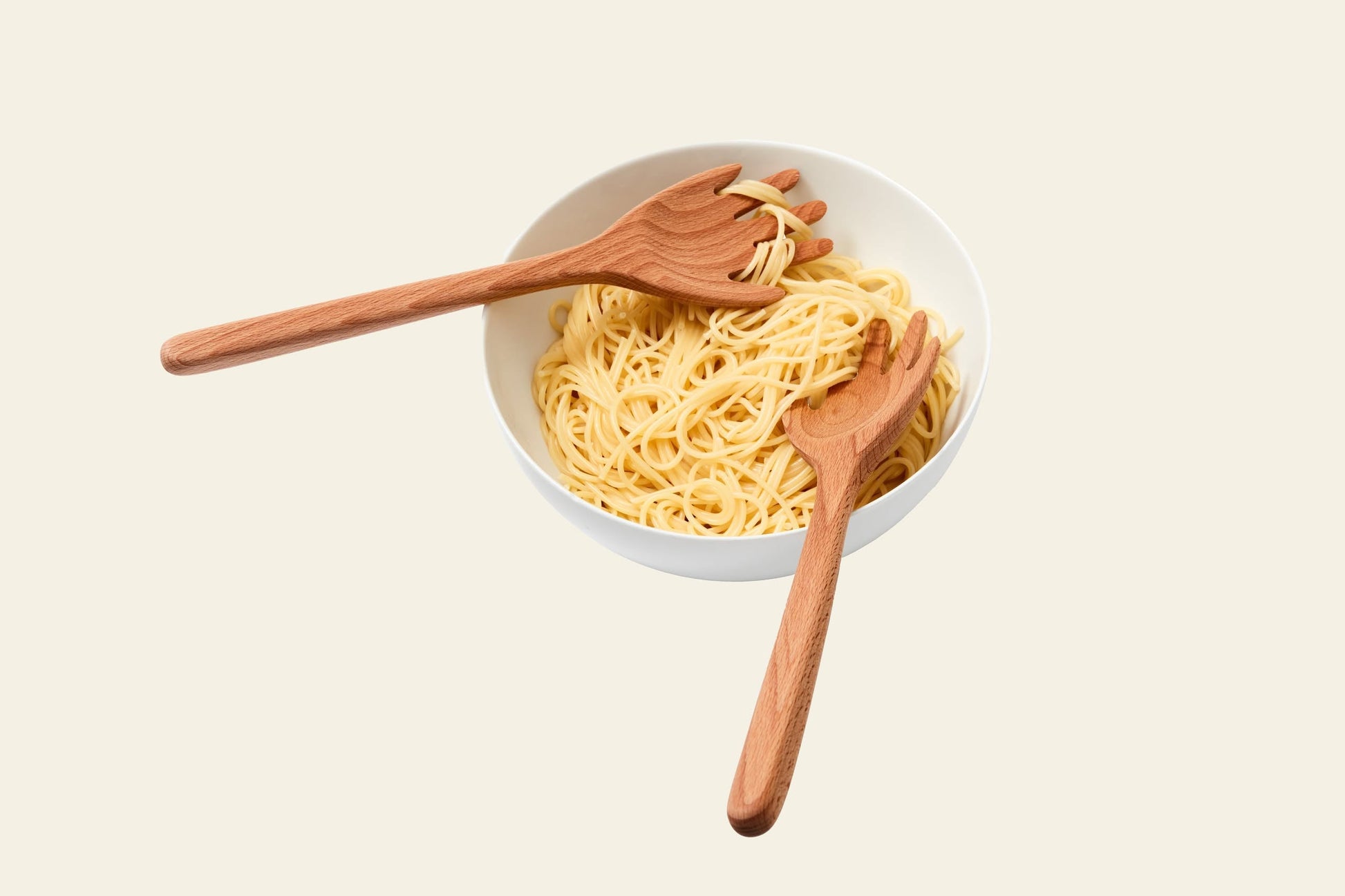 A white bowl of plain spaghetti is topped with Areaware Serving Friends - Hands by Areaware, two playful wooden serving spoons that enhance the dining experience against a light background.