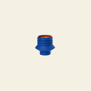 The Areaware Strata Plant Vessel by Areaware is a small, blue cylindrical ceramic planter with ridged sides, a flared middle, and a brown inner top. It’s shown against a simple light beige background.