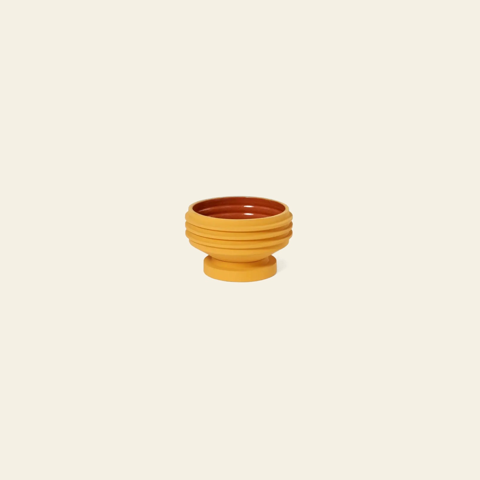 The Areaware Strata Plant Vessel by Areaware features a sculptural design with a mustard yellow ribbed exterior and brown interior, set on a matching pedestal, reminiscent of Simone Brewster’s style.