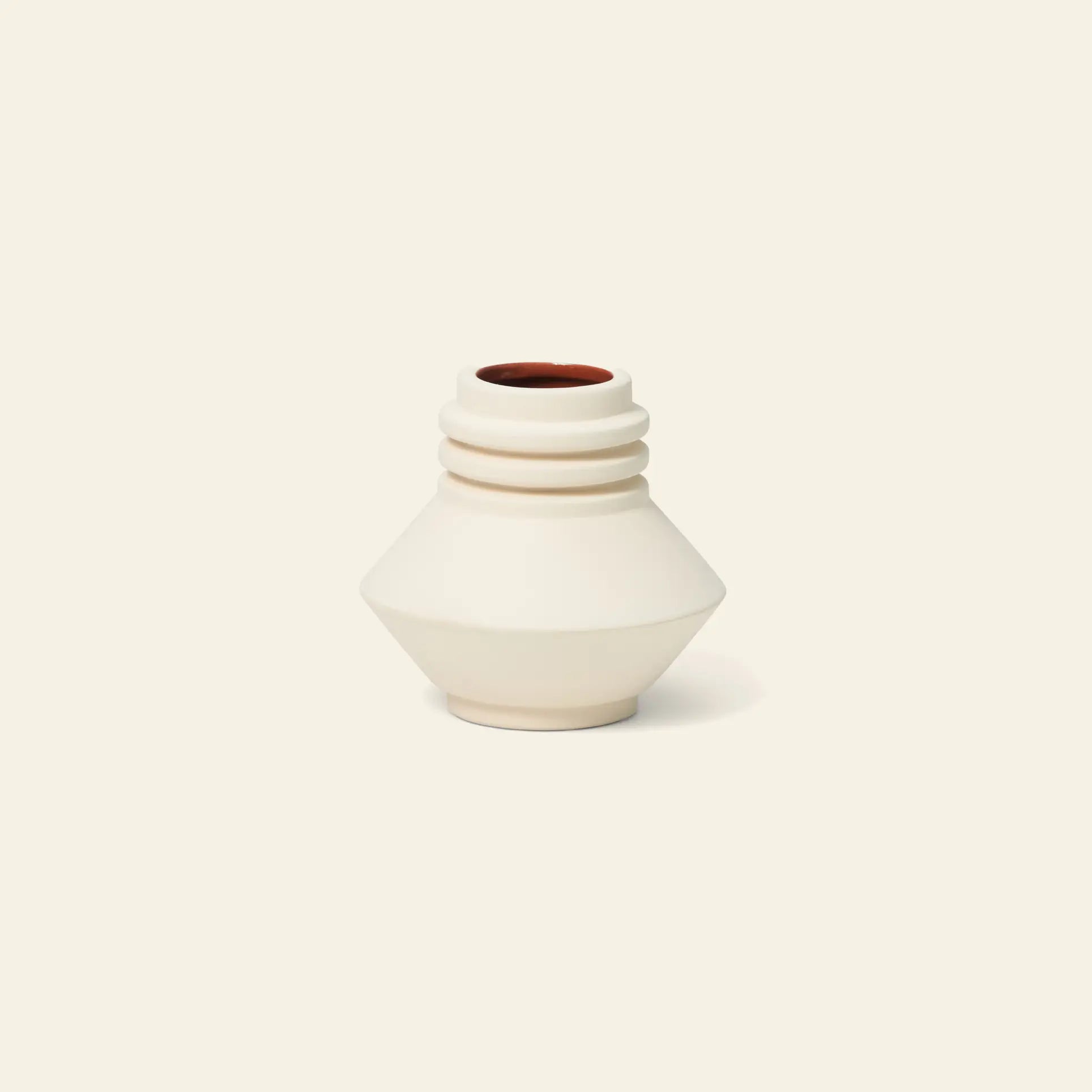 The Areaware Strata Vase Mini by Areaware is a small, cream ceramic vase featuring a geometric, angular shape with three ridges by the narrow opening and a reddish-brown interior—perfect for adding sculptural style to any space. Shown on an off-white background.