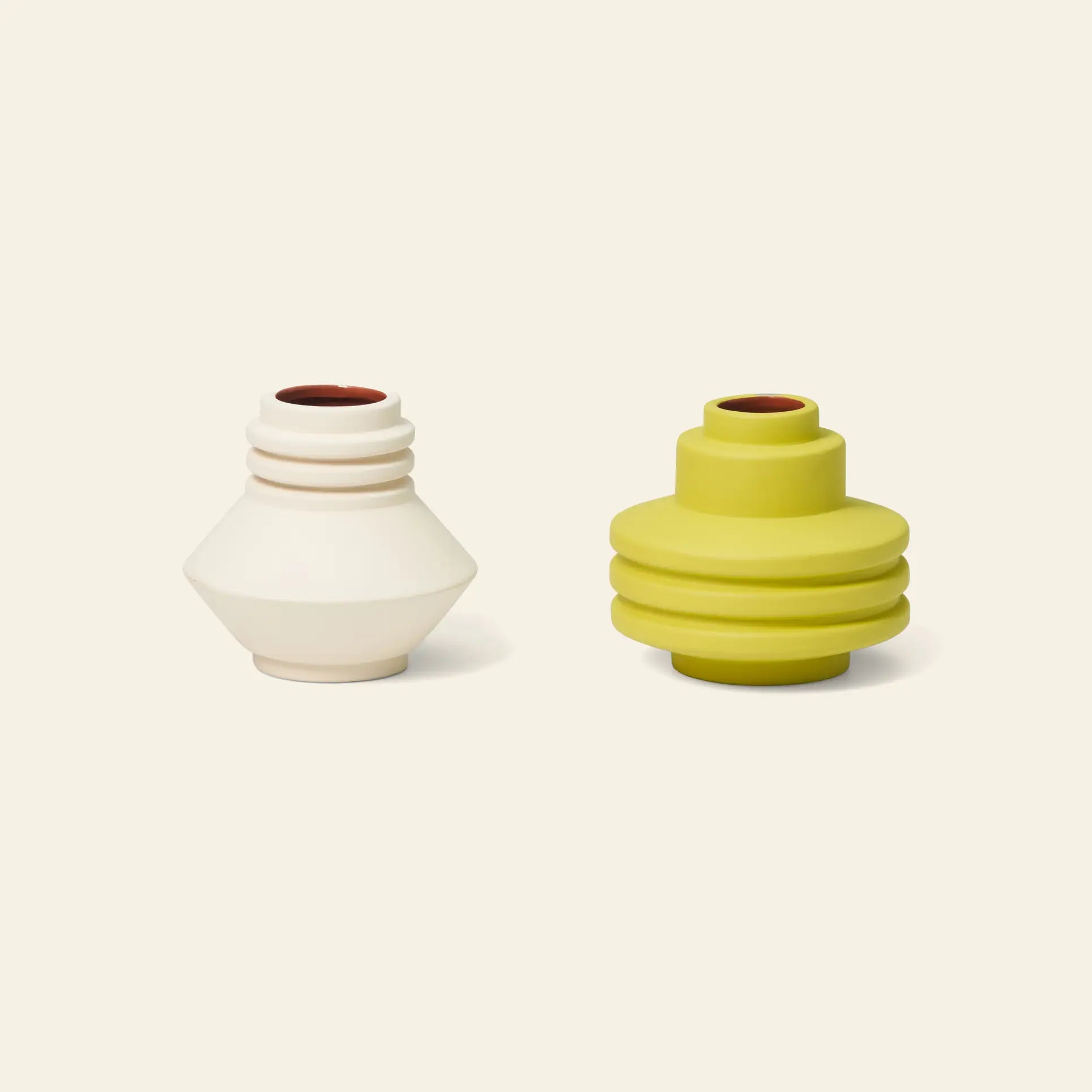 Two small, modern vases—a ridged off-white and a layered lime green—rest on a beige background, echoing sculptural forms and inspired by the Areaware Strata Vase Mini designs by Areaware.
