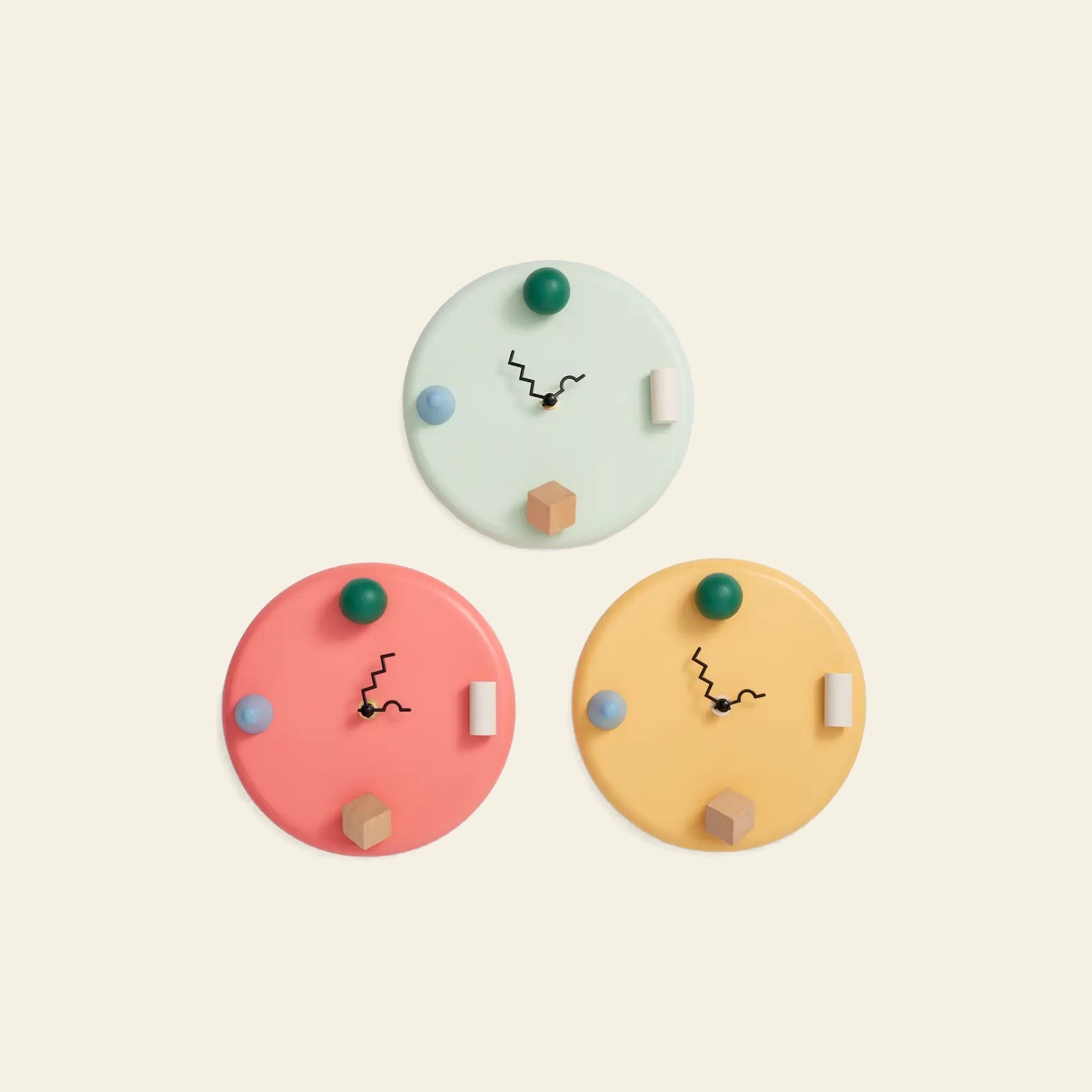 Three Areaware Wall Clocks by Areaware in pastel green, pink, and yellow have black zigzag hands and geometric hour markers, arranged triangularly on a plain light background for a whimsical timekeeping accent.