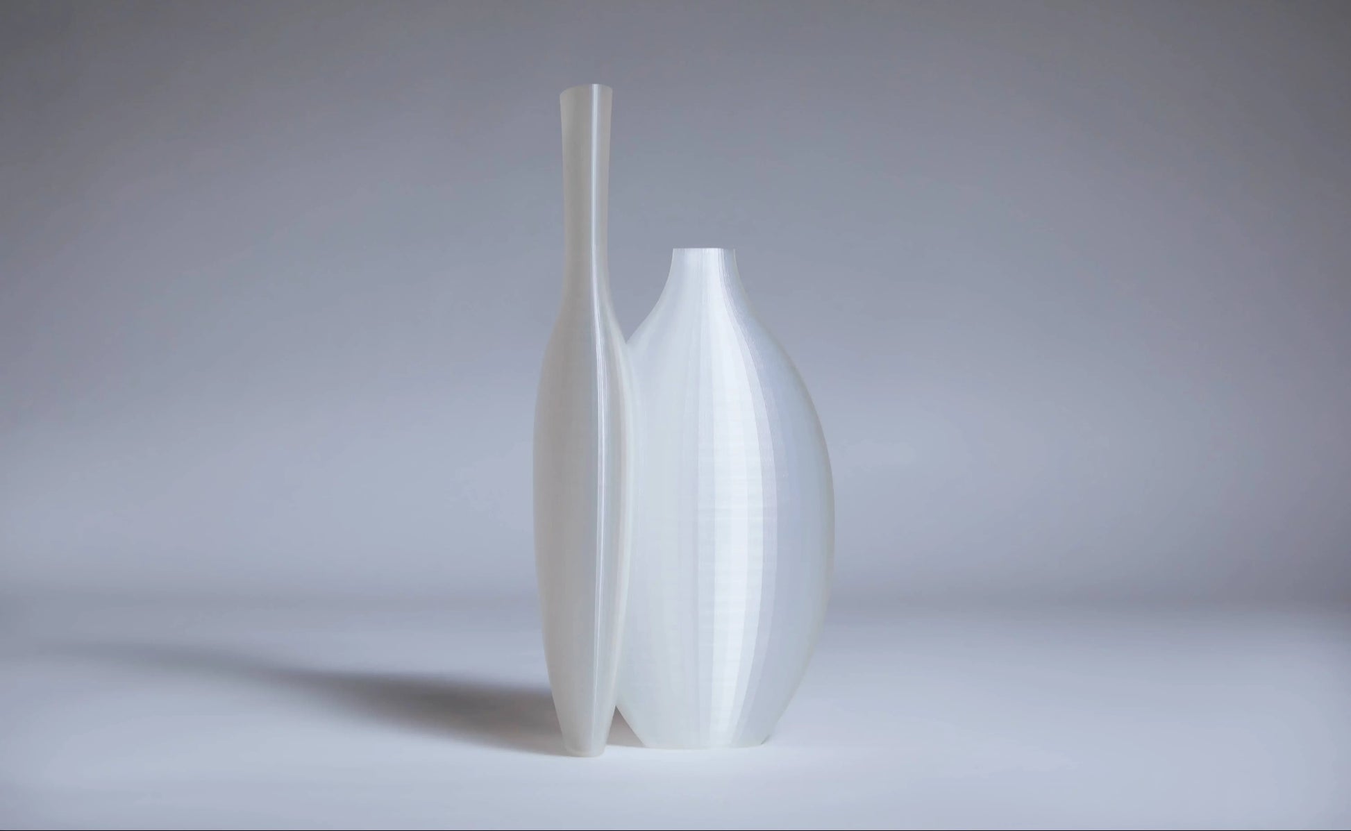 Two translucent white Argot Studio Double Vessels by Argot Studio stand side by side, their smooth forms offering a fresh take on minimalist design against a soft, neutral background.