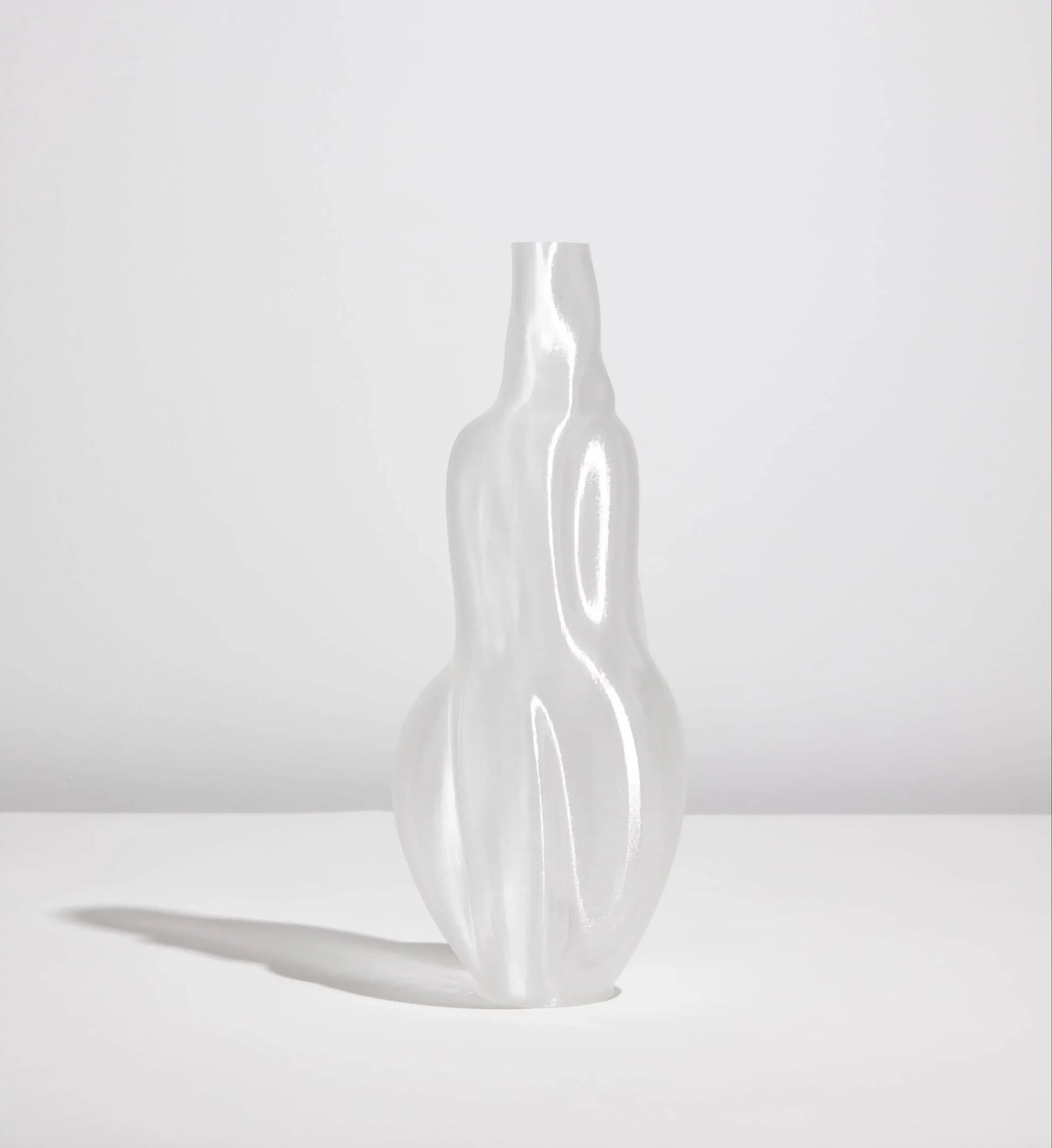 The Argot Studio Éson Vessel, Medium—a translucent, sculptural 3D-printed vase by Argot Studio with smooth, undulating curves—stands on a flat white surface and casts a soft shadow against a light gray background.
