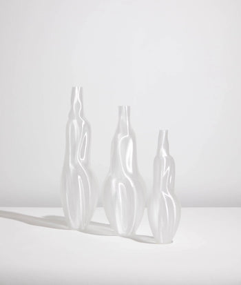 Three Argot Studio Éson Vessel, Medium vases by Argot Studio, featuring tall glossy white abstract curves, stand side by side on a white surface with soft shadows against a plain background.