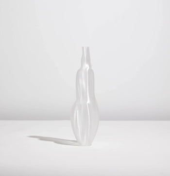 The Argot Studio Éson Vessel, Small—a matte, translucent vase with an abstract elongated form—sits on a white surface against a light gray background, casting a soft left shadow and offering a modern take on organic fluid design.