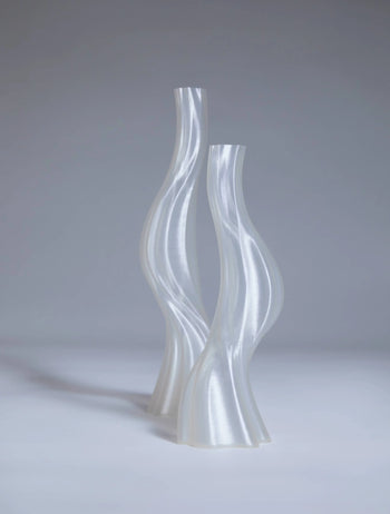 Two tall, translucent vases—Argot Studio Les Hortenses Vases (Small) by Argot Studio—stand side by side on a neutral gray surface, showcasing a glossy, contemporary reinterpretation made from 3D printed material.